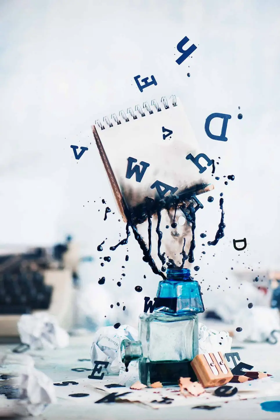 Notebook with blank pages and spilled ink flying above inkwells with scattered black letters on a light background